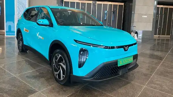 A cyan-colored Green SM VinFast Limo Green electric taxi navigating a modern street in New Delhi, representing the brand's entry into India.