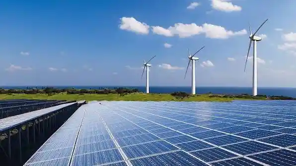 A sprawling solar farm and wind turbines operating in rural India under a clear sky.