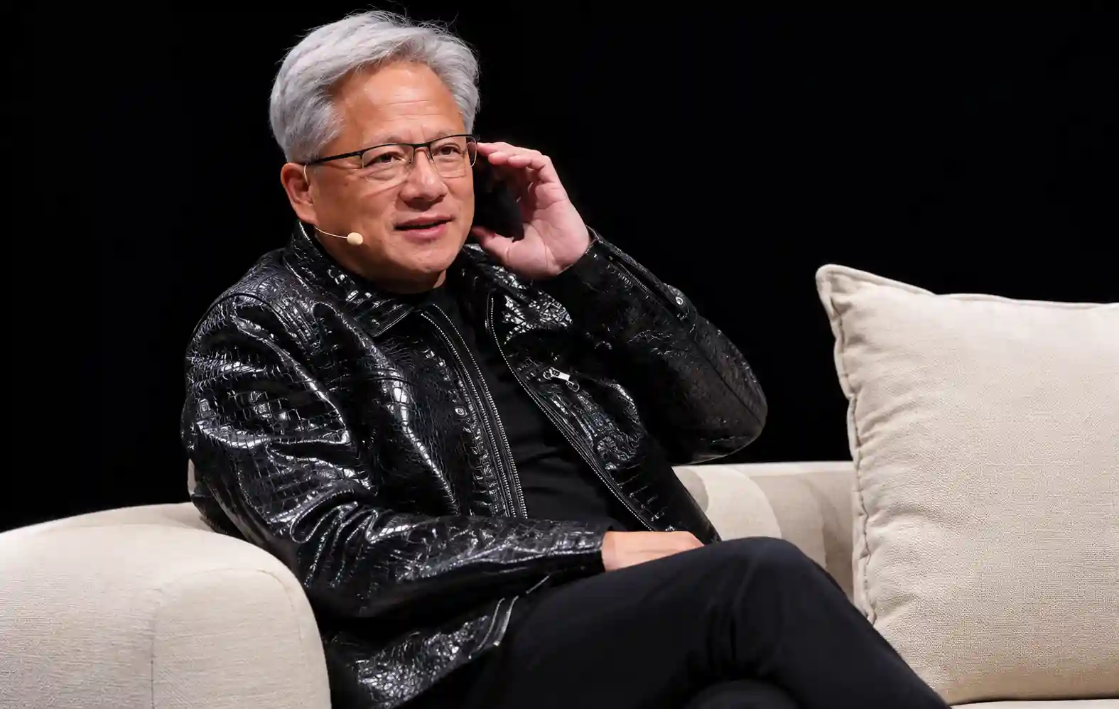 Nvidia CEO Jensen Huang holding a phone to a microphone on stage.